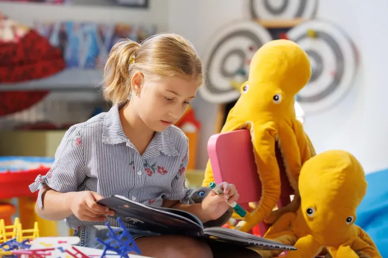 A girl reading a book next to two plush squids