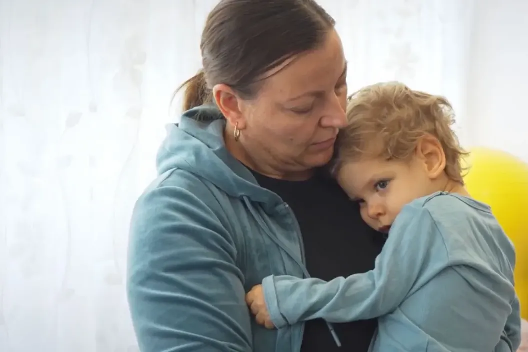 Un copil la pieptul mamei sale care &icirc;l &icirc;mbrățișează.