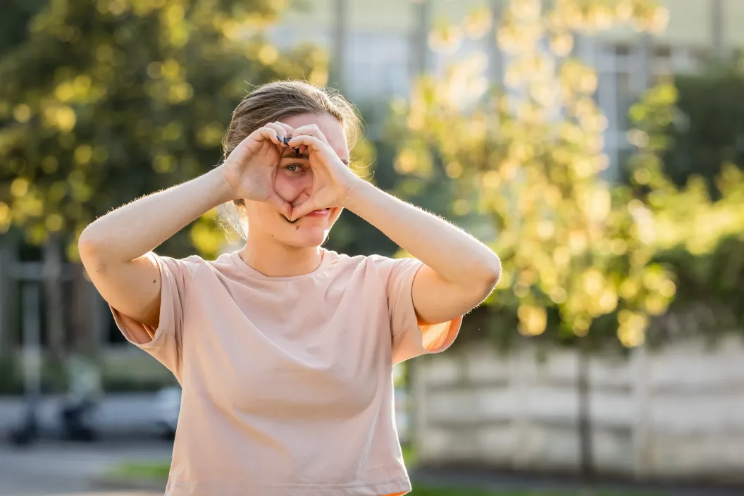 Adolescentă care arată o inimioară la cameră.