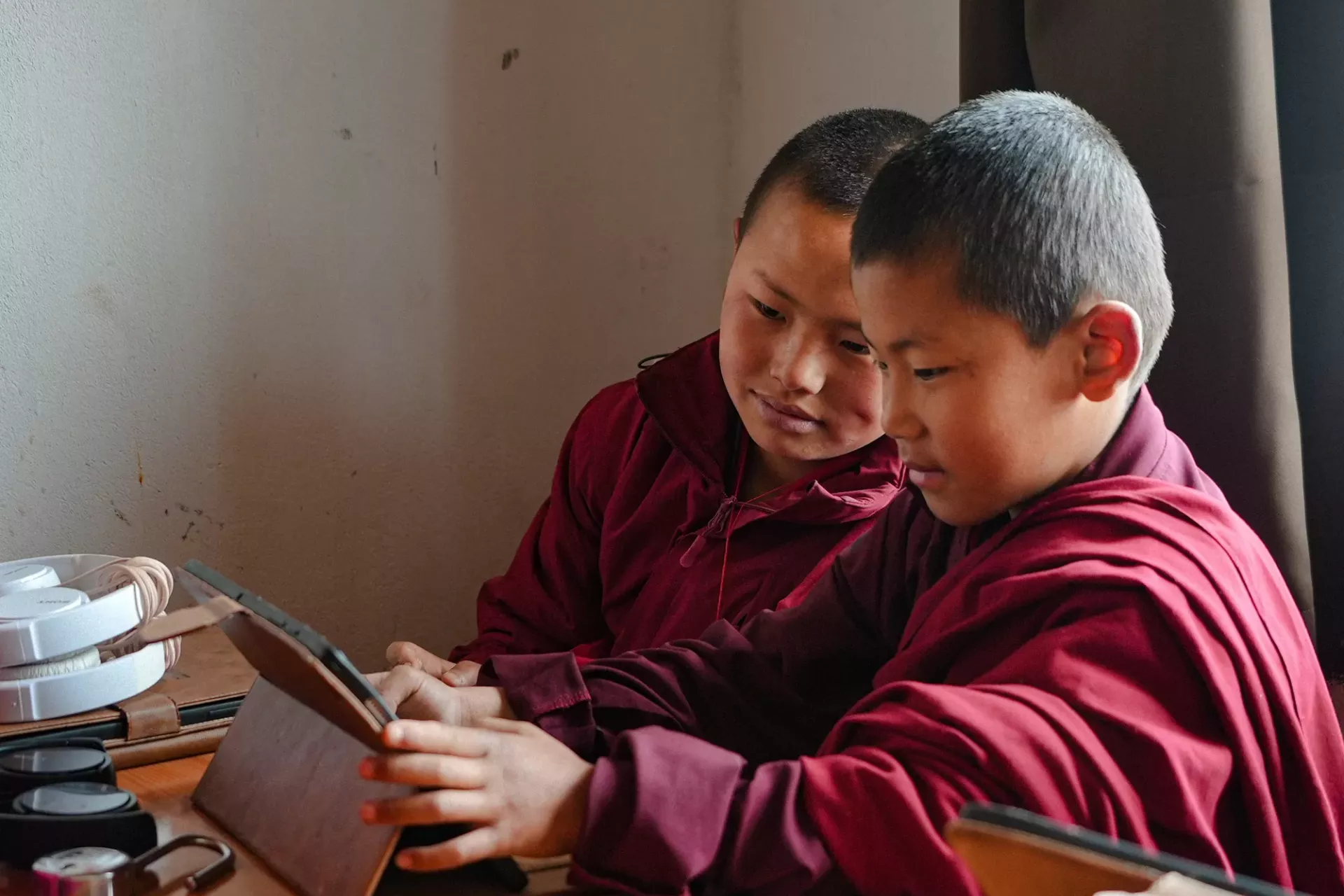 Two young student monks in red robes consult around as the share a tablet for learning