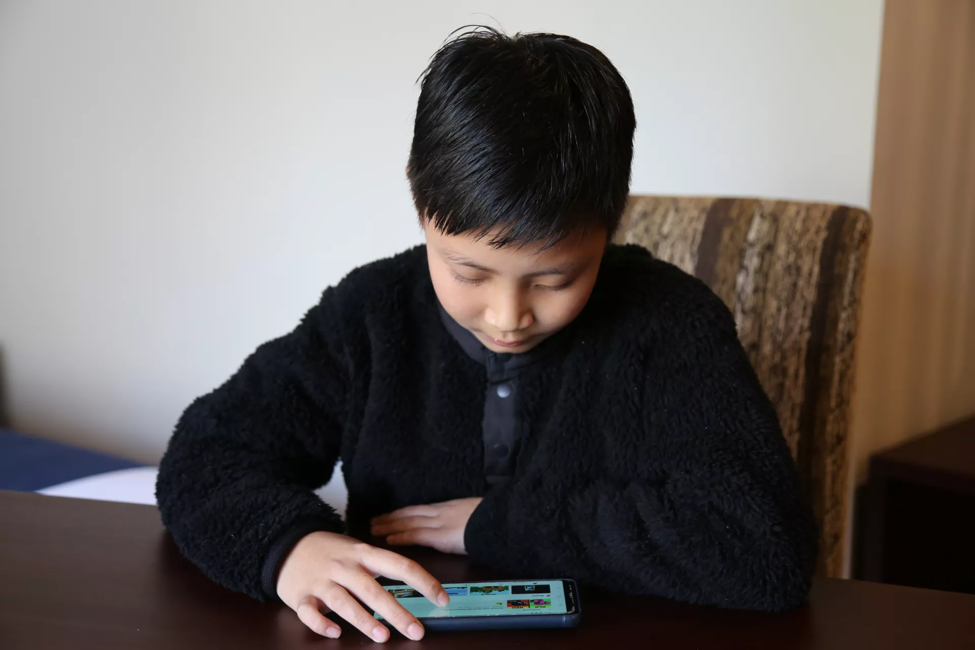Seven-year-old Kelzang Yeshi watches a cartoon on a cell phone at home.
