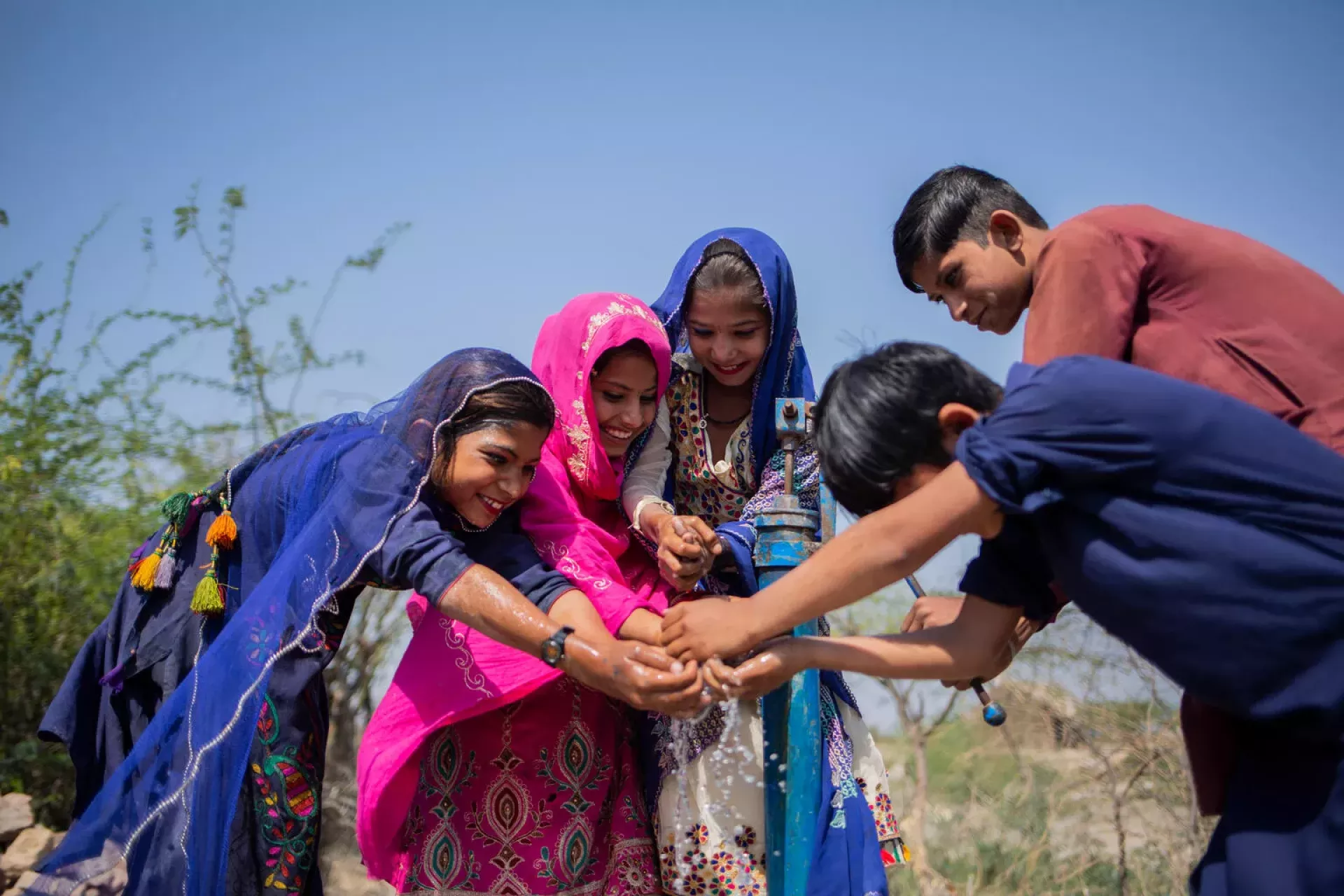 Three girls and two boys play with water from a hand-pump in Pakistan