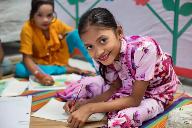 A girl smiles as she draws on a paper.