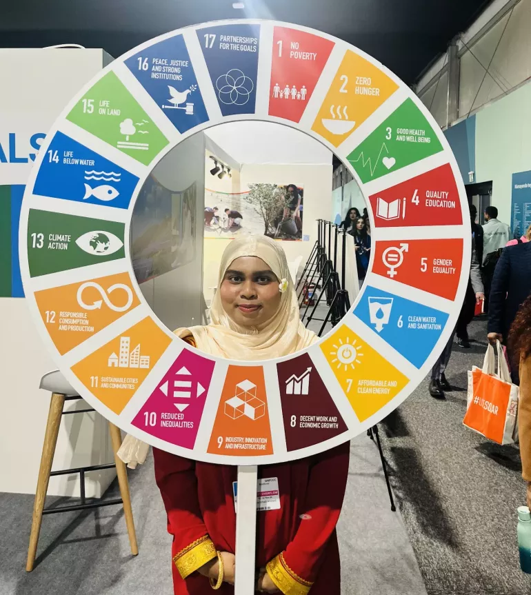 Fathima, a young female COP29 delegate standing behind a circle of Sustainable Development Goals (SDGs). 