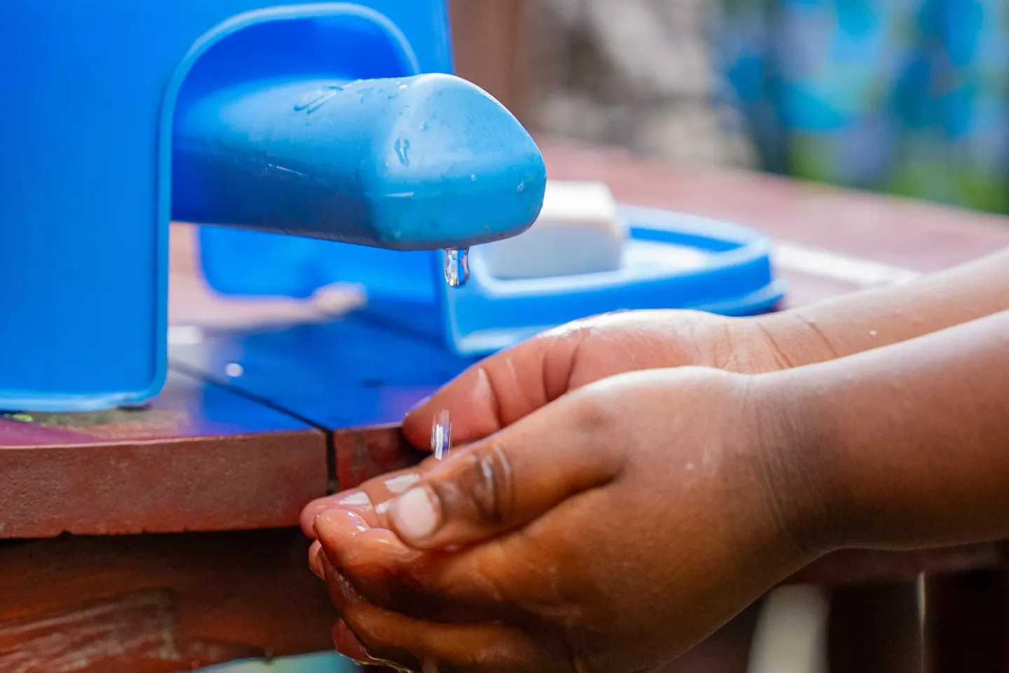 Water dripping in a child's hands from a blue plastic tap.