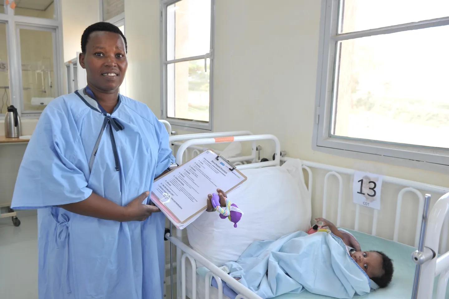 Jacqueline Mukawiringiye, Head Nurse in the neonatology ward at Rwanda's Gahini Hospital, stands in her scrubs wit ha clipboard next to the bed of a prematurely born baby, now recovering and in good health.