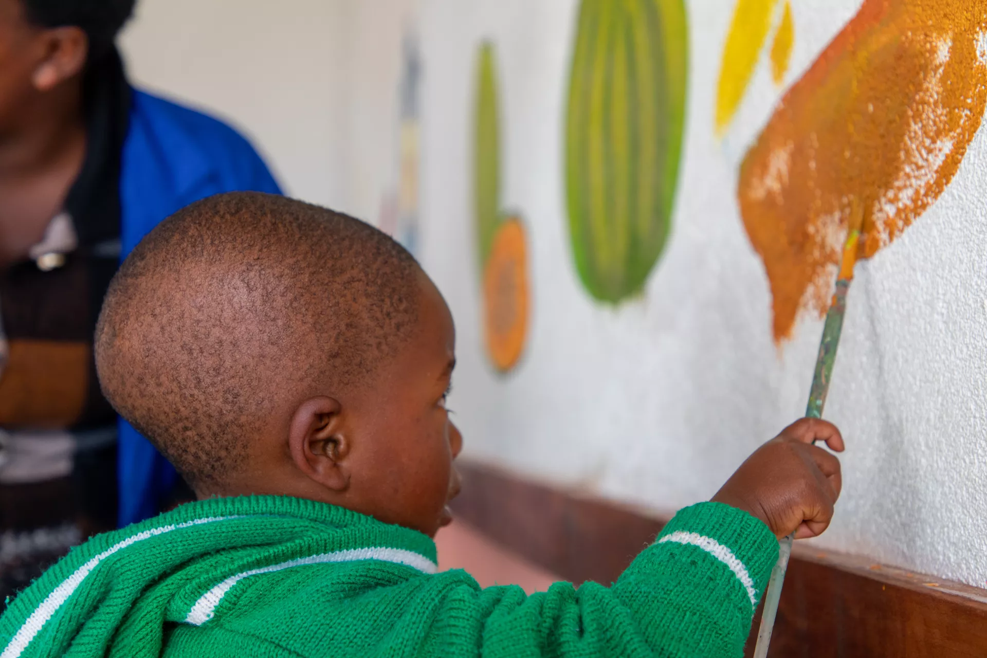 A little boy at the Rutsiro Tea Plantation ECD centre paints a mural of fruits with UNICEF and local artists.