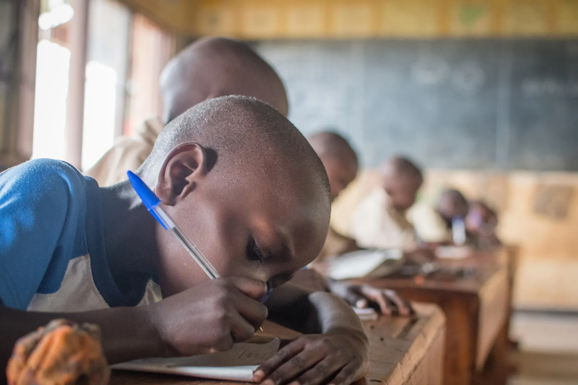 A boy in primary school in Rwanda writes studiously at his desk.