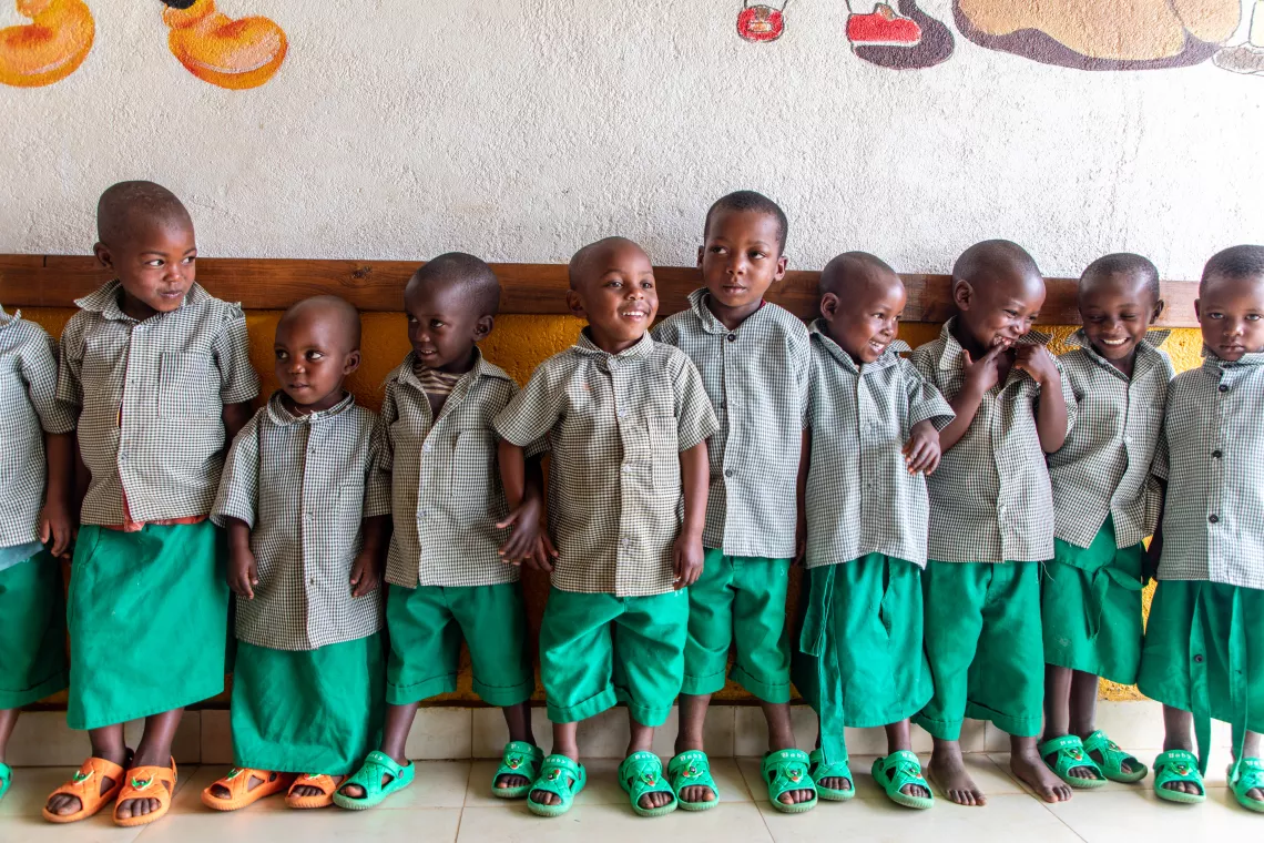 Children between age 3 and 6 line up against a wall at their day care centre, smiling and laughing.