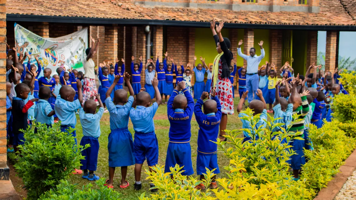 Children in royal blue uniforms play games with their caregivers at the UNICEF-supported Gikomero Early Childhood Development Centre in Rwanda.