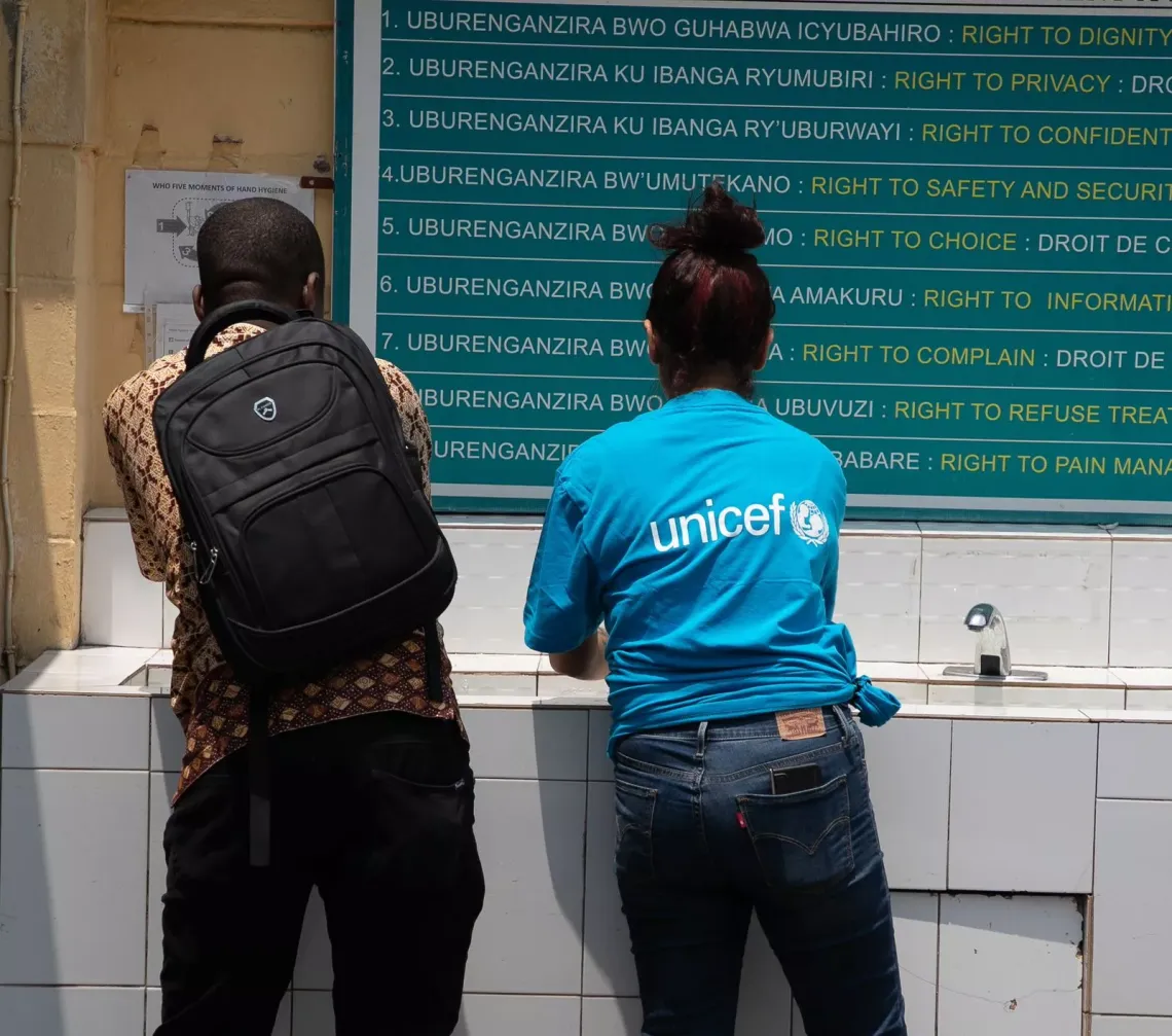 A man and a woman wearing a UNICEF-branded t-shirt wash their hands at a handwashing station.