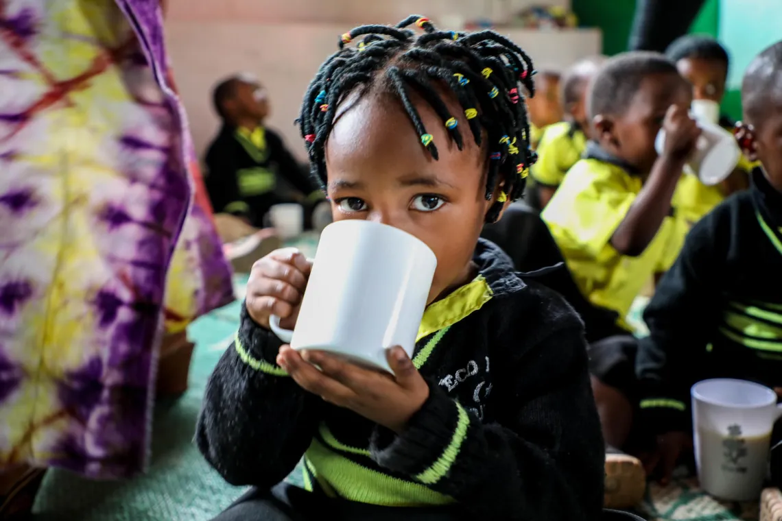 A young girl in an ECD centre drinks a mug of milk