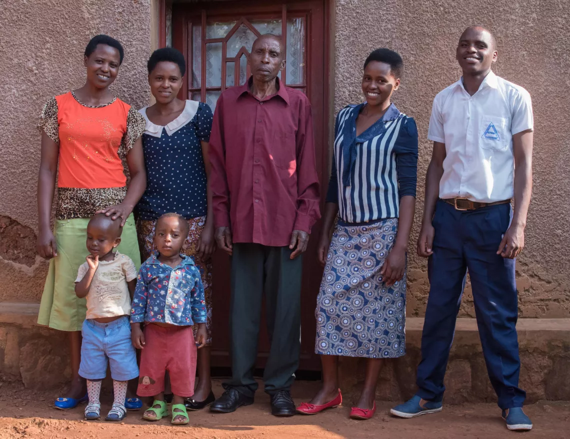 Standing with his family outside of their rural home in Rwanda, Adrien smiles proudly in his white school uniform. He will be the first of his family's nine children to complete secondary school.