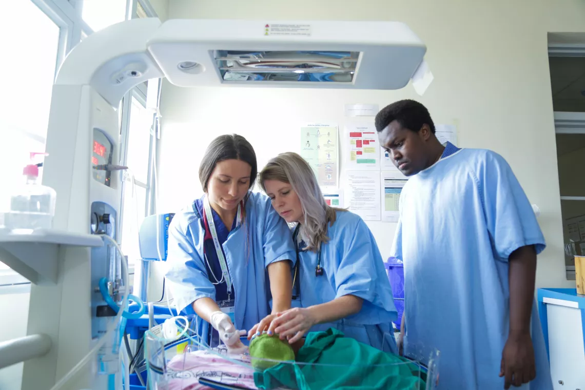 Dr. Evelyn Little, center, and nurse Lizzy Smeaton-Russell, left, work with a new doctor at Gahini Hospital to care for a newborn resting in an incubator.