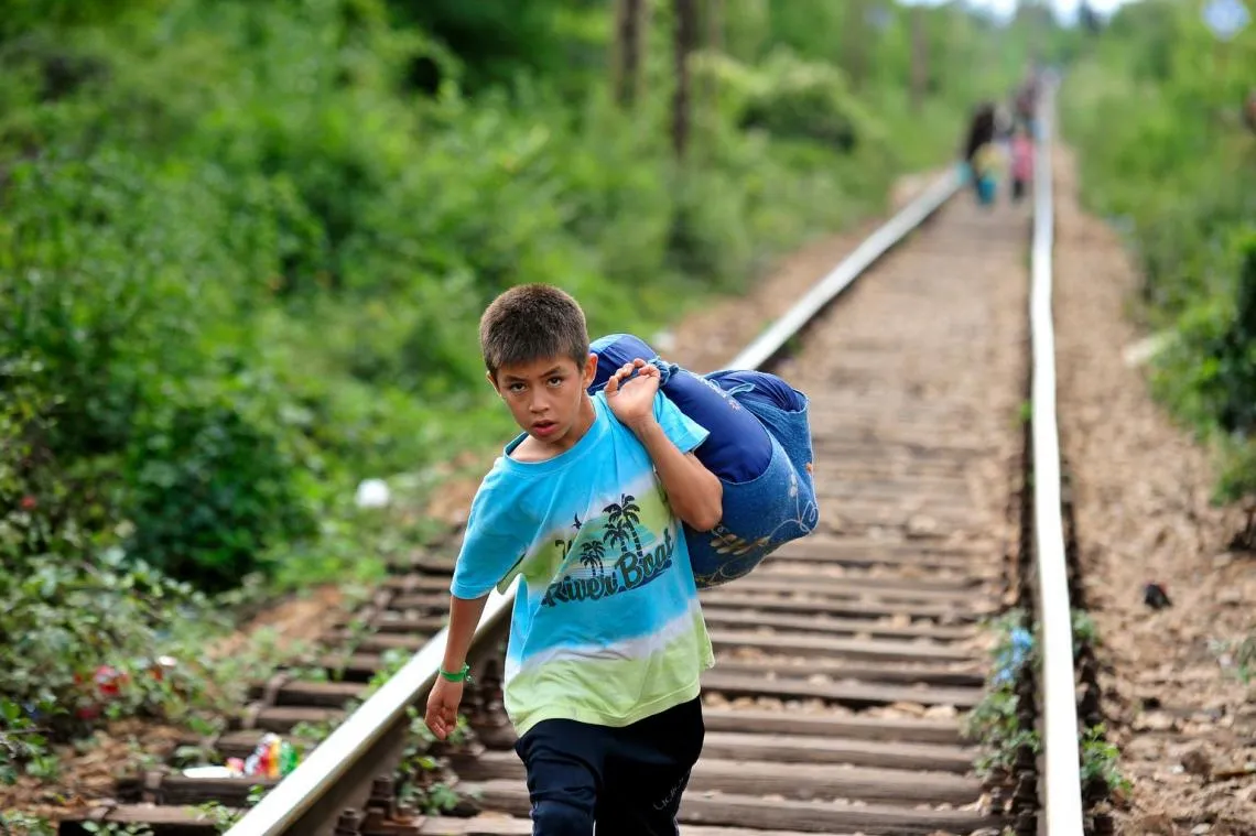 A boy carries his belongings in a large cloth bag as he walks on railway tracks to cross from the former Yugoslav Republic of Macedonia into Serbia.