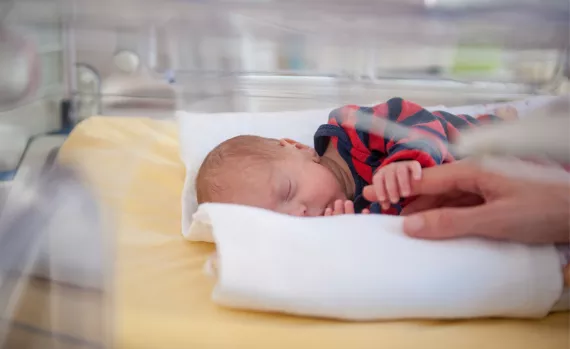 a baby in an incubator holding mom's finger
