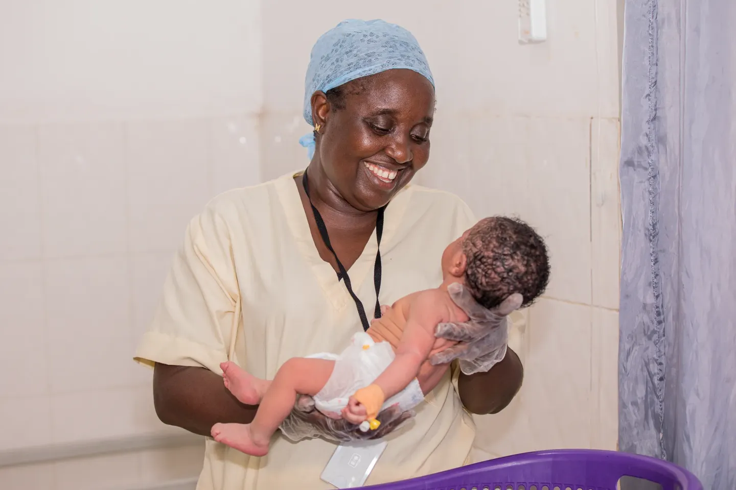 Victoria Bintu Fofanah smiles as she holds a newborn at Makeni Government Hospital in Sierra Leone. As a midwife receiving specialised training in neonatal nursing, she is strengthening her skills to provide better care for newborns.  