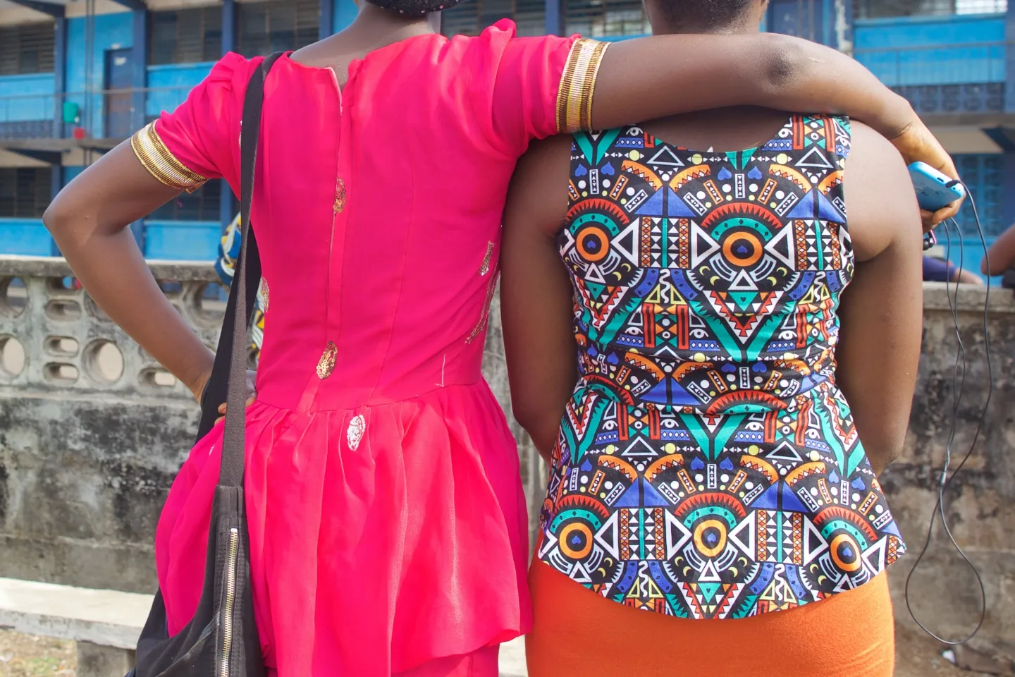 Two girls stand by the fence of a school in Freetown