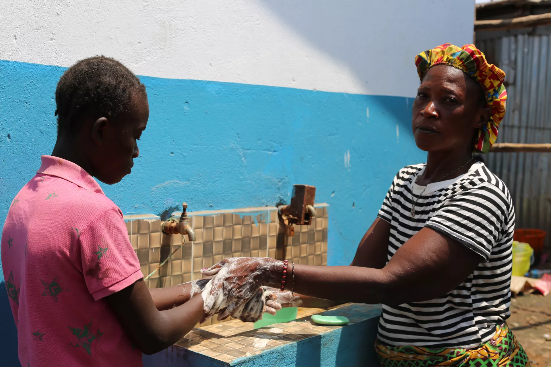 Agrandmother helps her granddaughter to wash her hands properly with soap