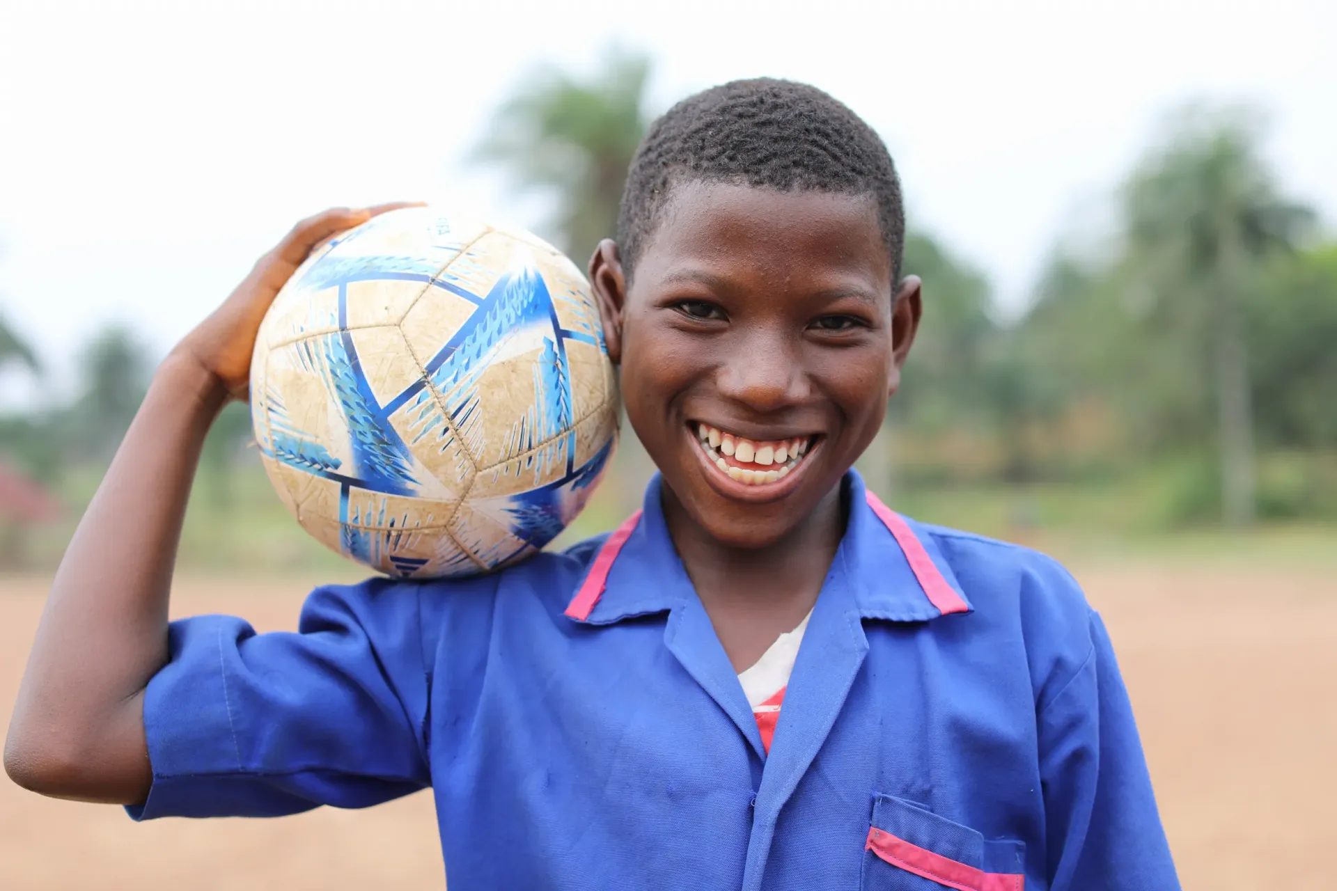 A boy is standing outside on the school premises holding a ball.