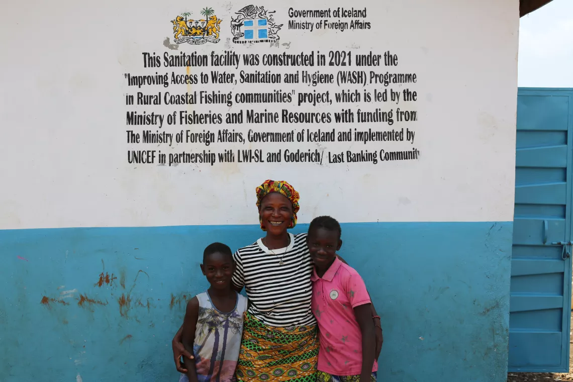 A woman and her two grandchildren stand in front of a toilet in Freetown