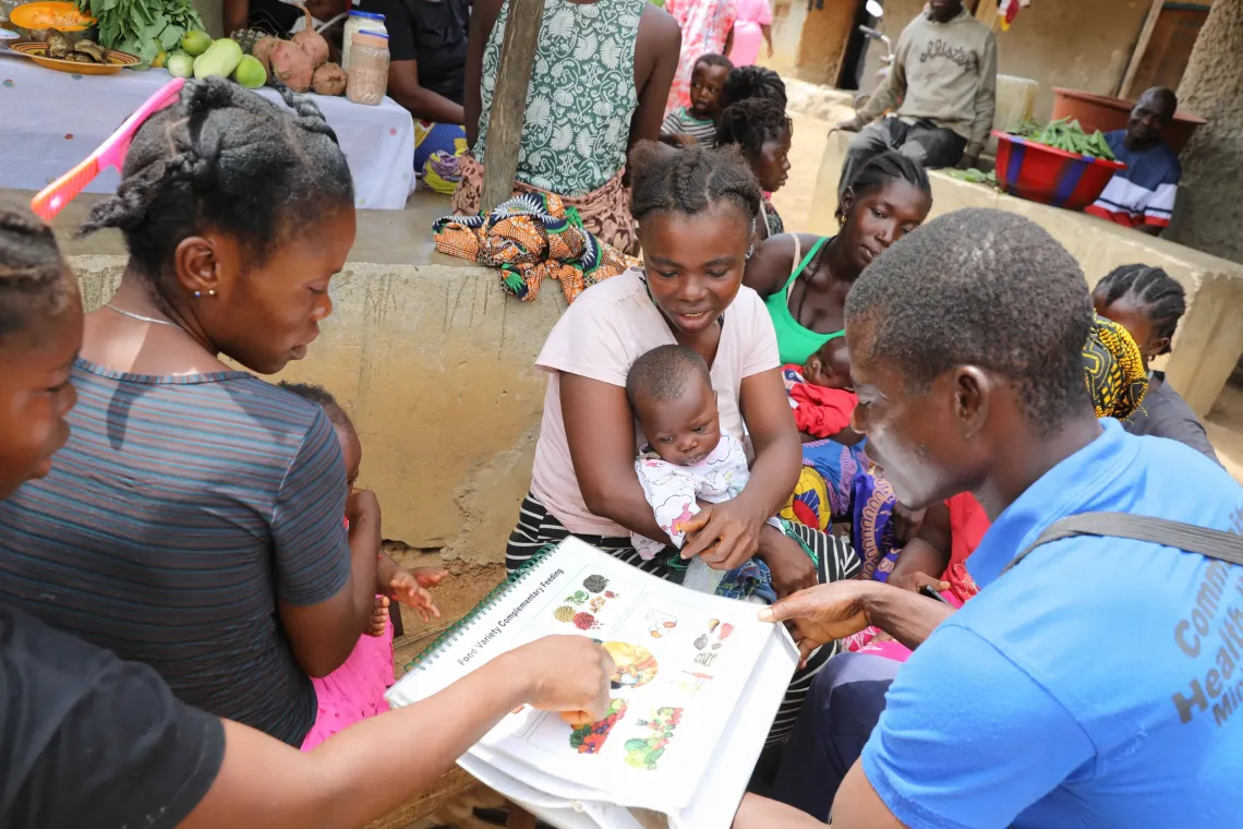 Mohamed Kamara educates mothers on the benefits of good nutrition during a community outreach session in Njagbahun village, Moyamba, using a UNICEF-supplied manual