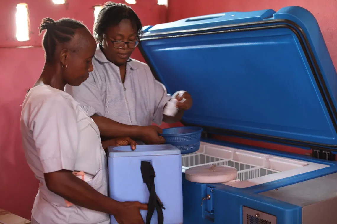 Jenevia is assisted by another health worker to take vaccines from the solar powered refrigerator and pack them into a portable vaccine career in readiness for their outreach exercise