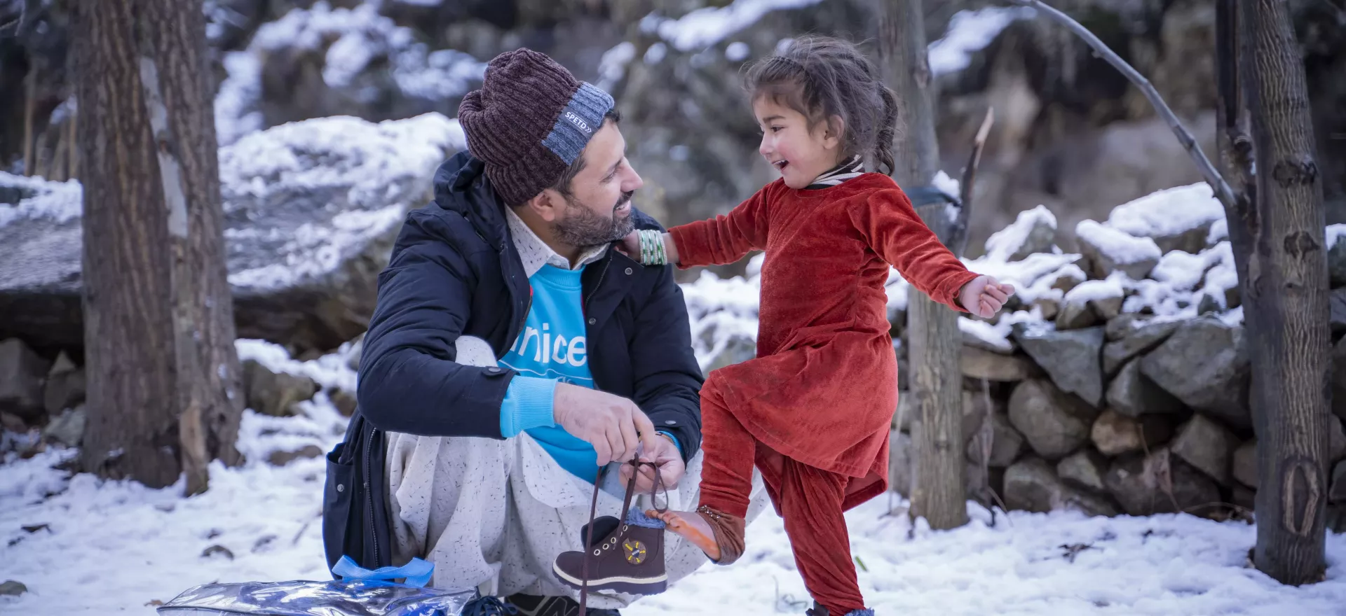 Un enfant met des chaussures neuves avec l&rsquo;aide d&rsquo;un agent de l&rsquo;UNICEF. Dans un paysage enneig&eacute;. 