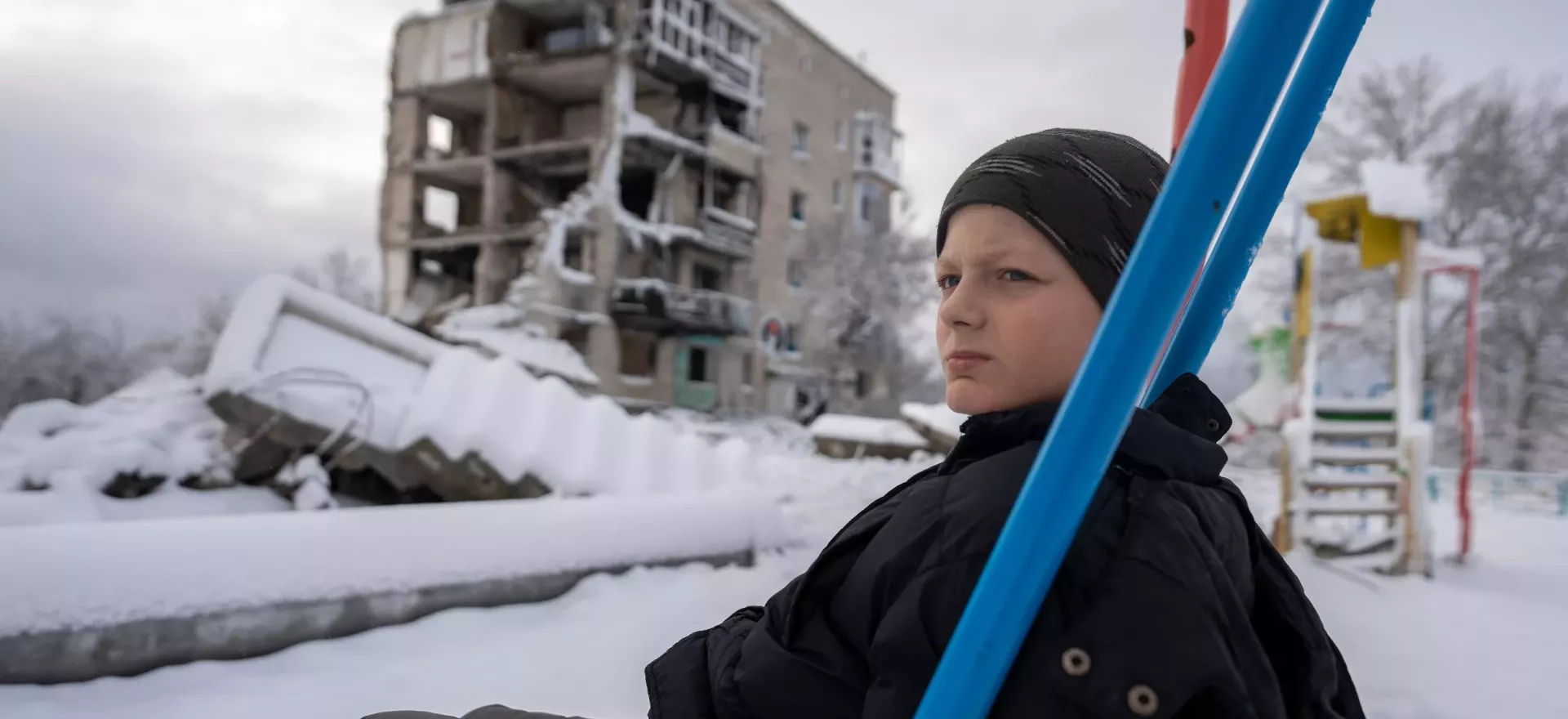 Ukraine. A boy wearing a winter jacket sits on a swing.