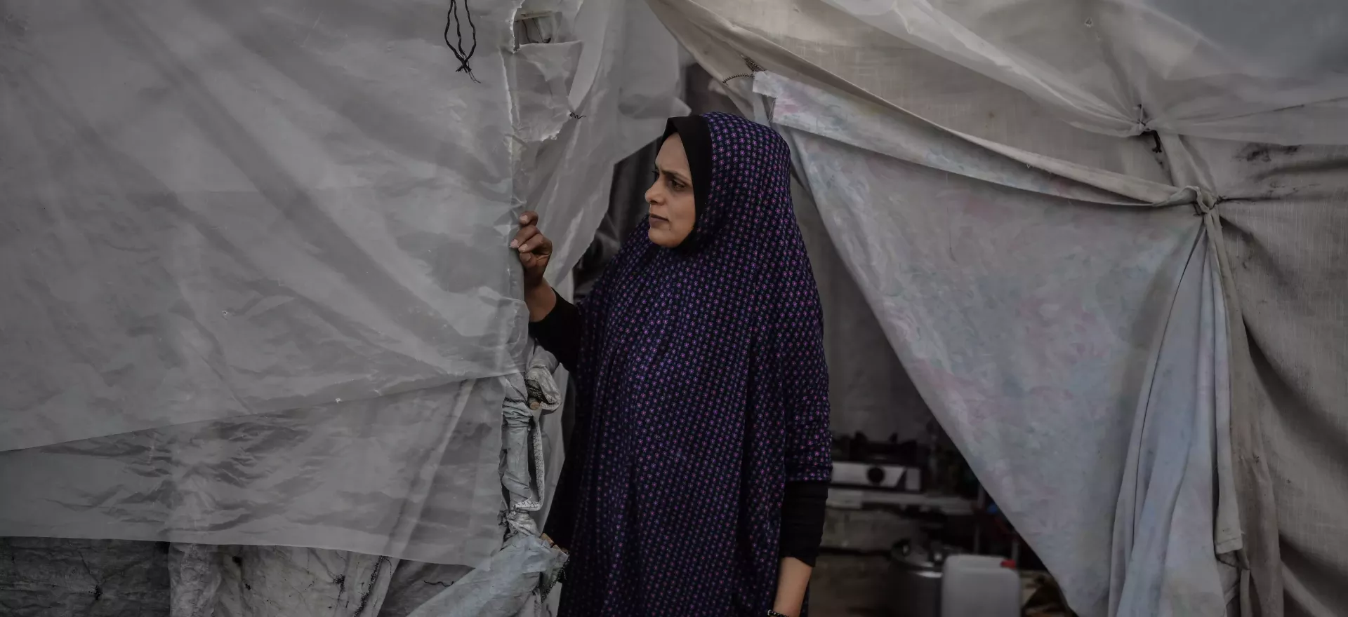 A woman stands in the doorway of a makeshift shelter.