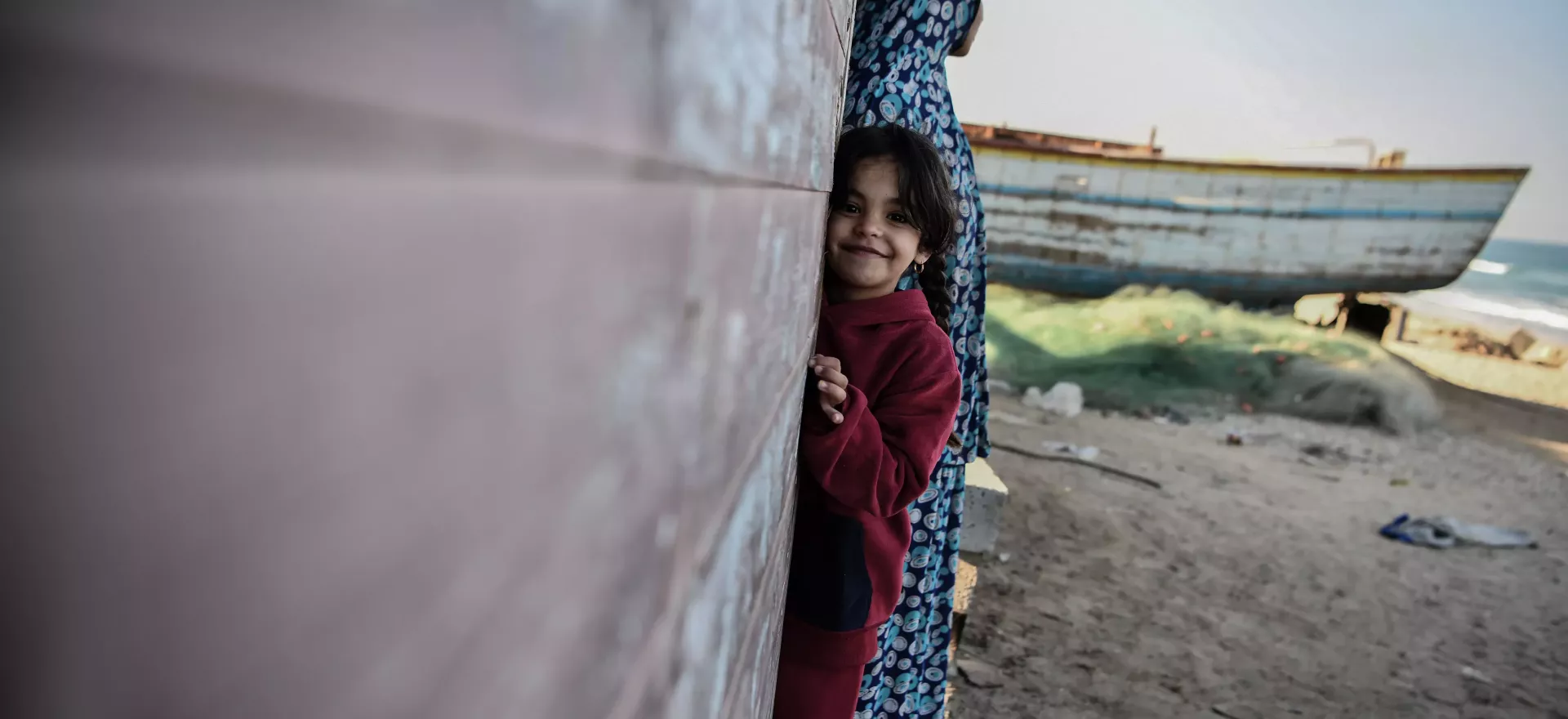 Una ni&ntilde;a se asoma a una puerta, sonriendo a la c&aacute;mara, con su madre a su lado mirando a lo lejos.