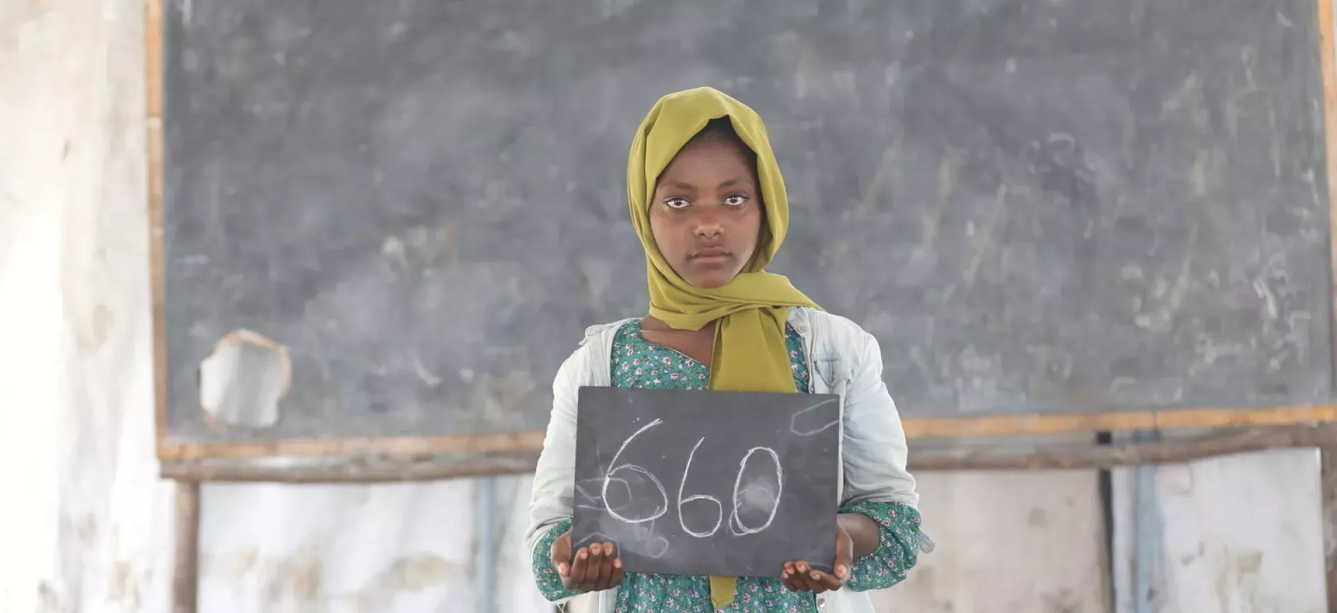 Ethiopia. A girl stands in an empty classroom holding a chalkboard showing how many days she has been out of school.