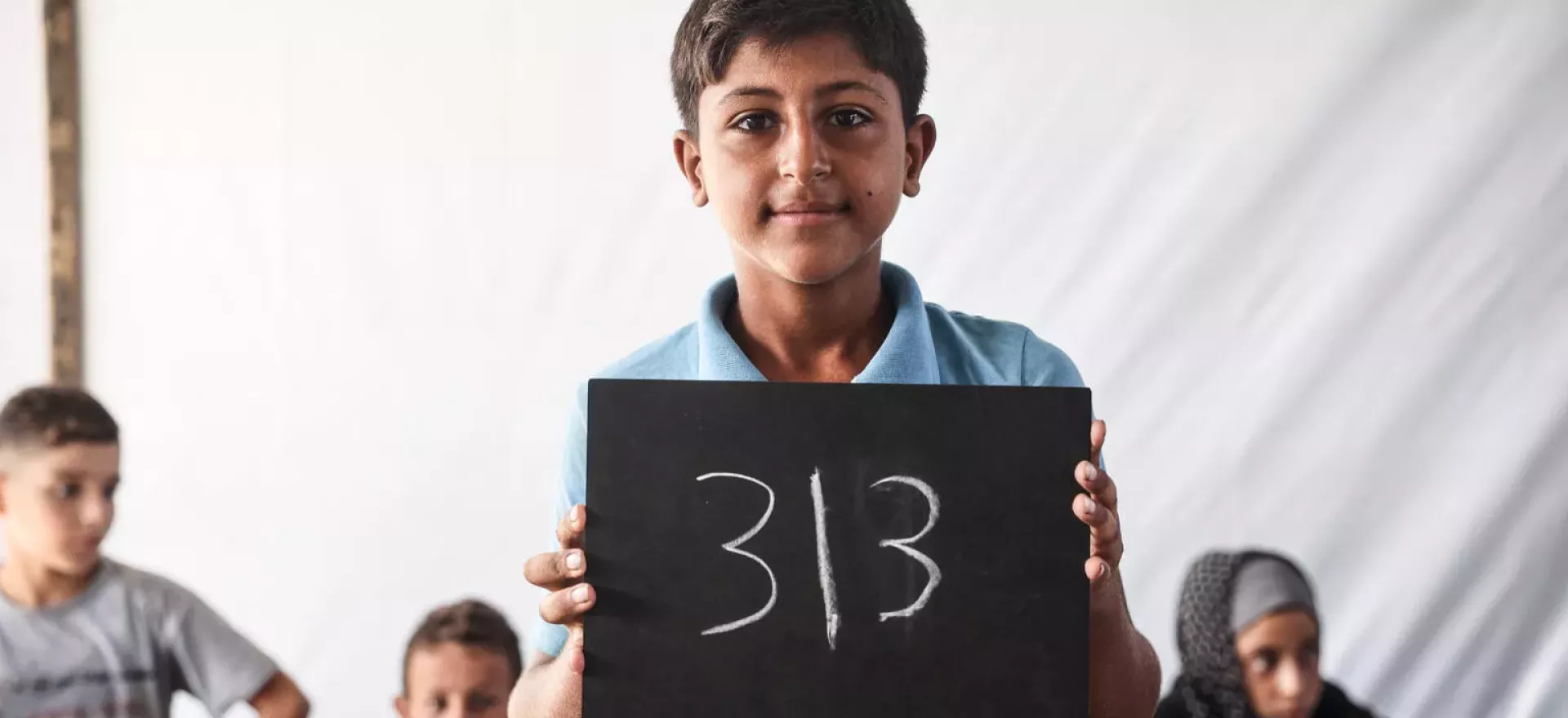 State of Palestine. A boy holds up a chalkboard with the number of days he has been out of school.