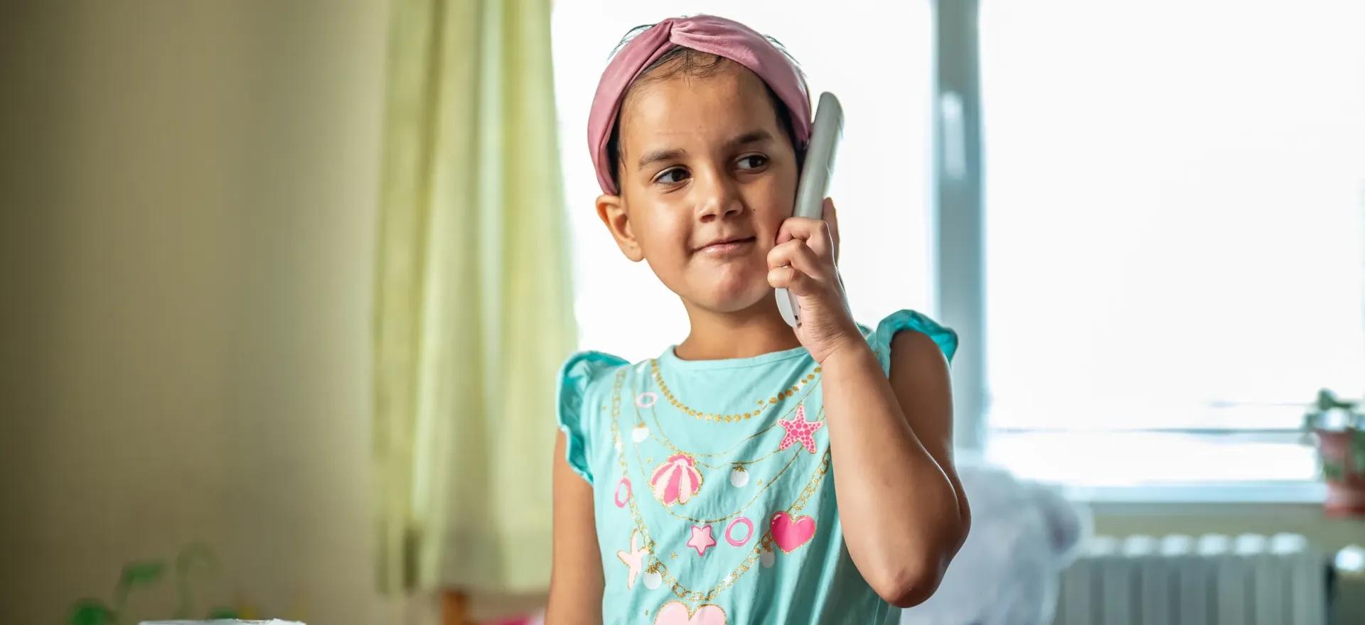 Sylvia, dress in a turquoise top and pink headband, plays in the Community Support Center in Burgas, Bulgaria.