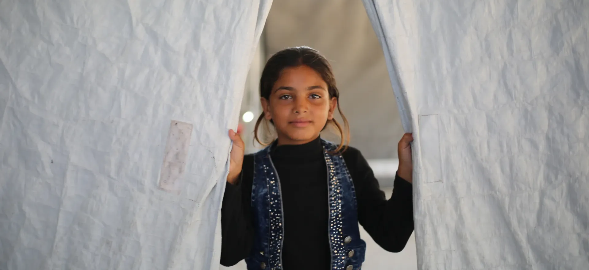 Gaza. A girl looks from between the flaps of a tent.