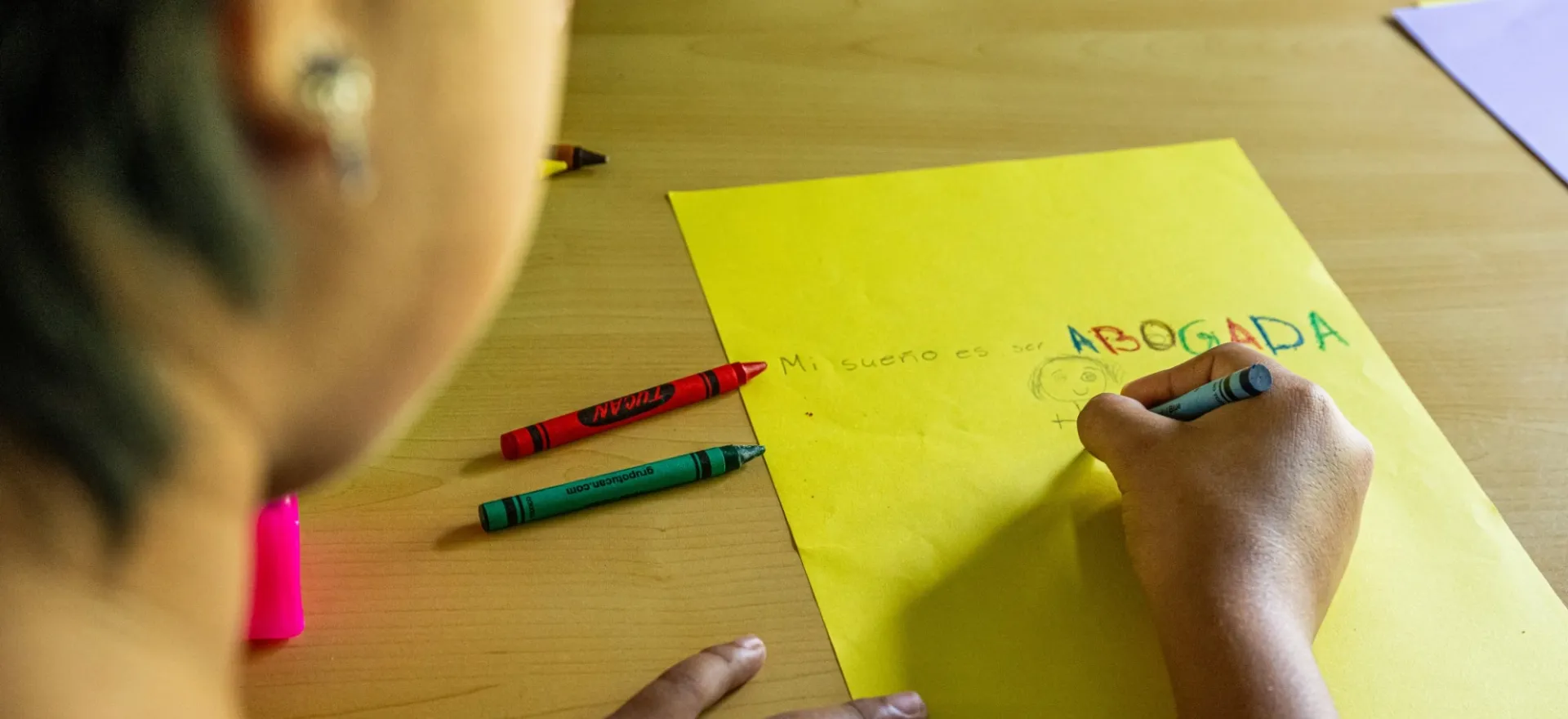 A girl with short, cropped hair draws a picture on a yellow sheet of paper.
