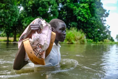 South Sudan. A girl holds up her books to keep them out of the floodwater on her way home from school.