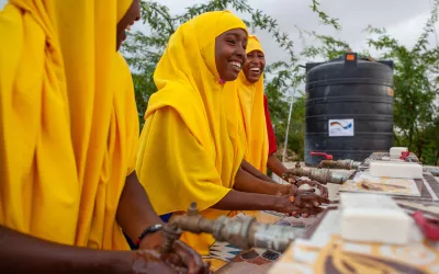 Three girls in bright yellow dress standing beside each other washing their hands