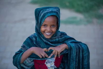 A young smiles from Sudan smiles brightly while making a heart shape with her hands.