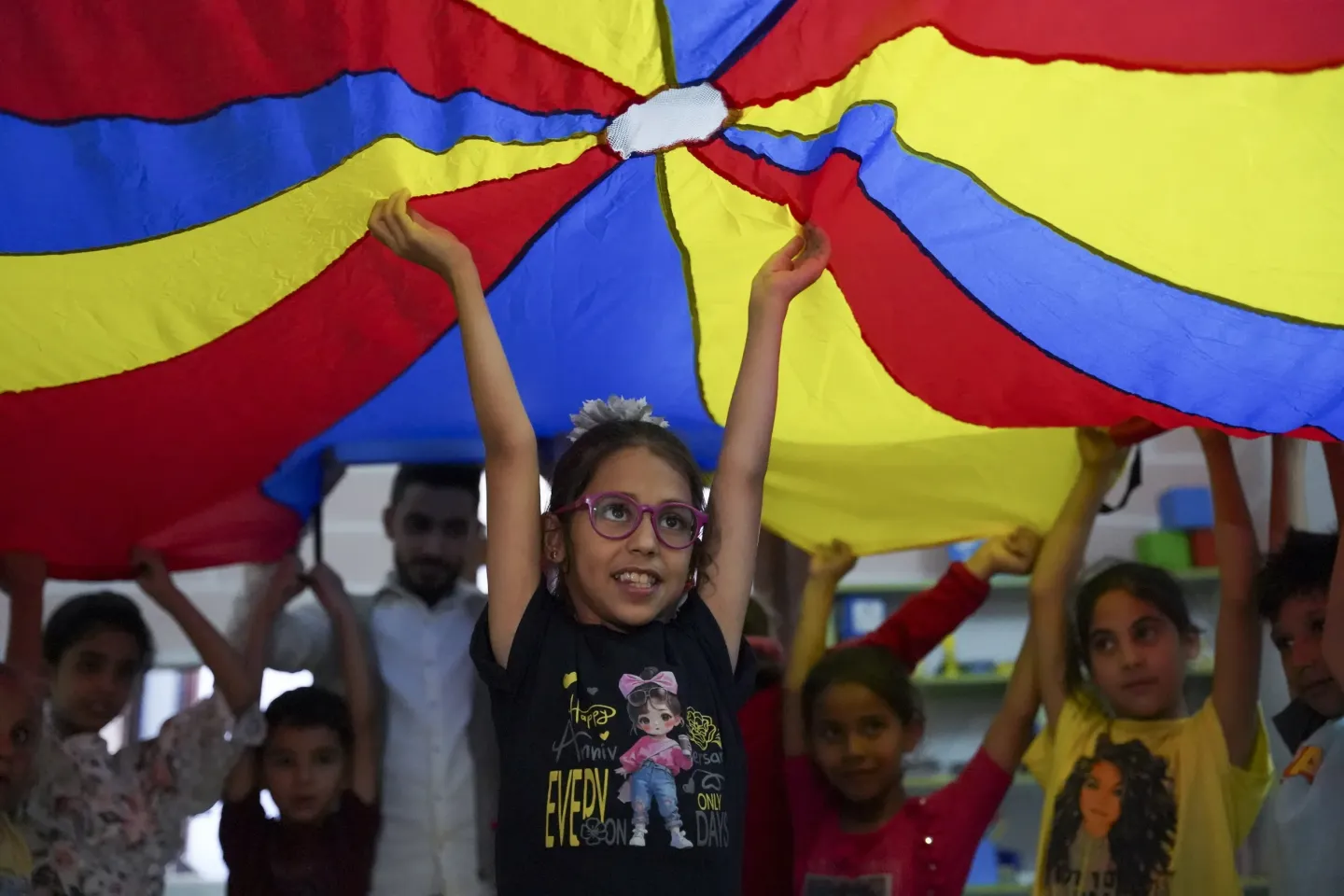 Children joyfully standing underneath and holding up a yellow blue and red flag