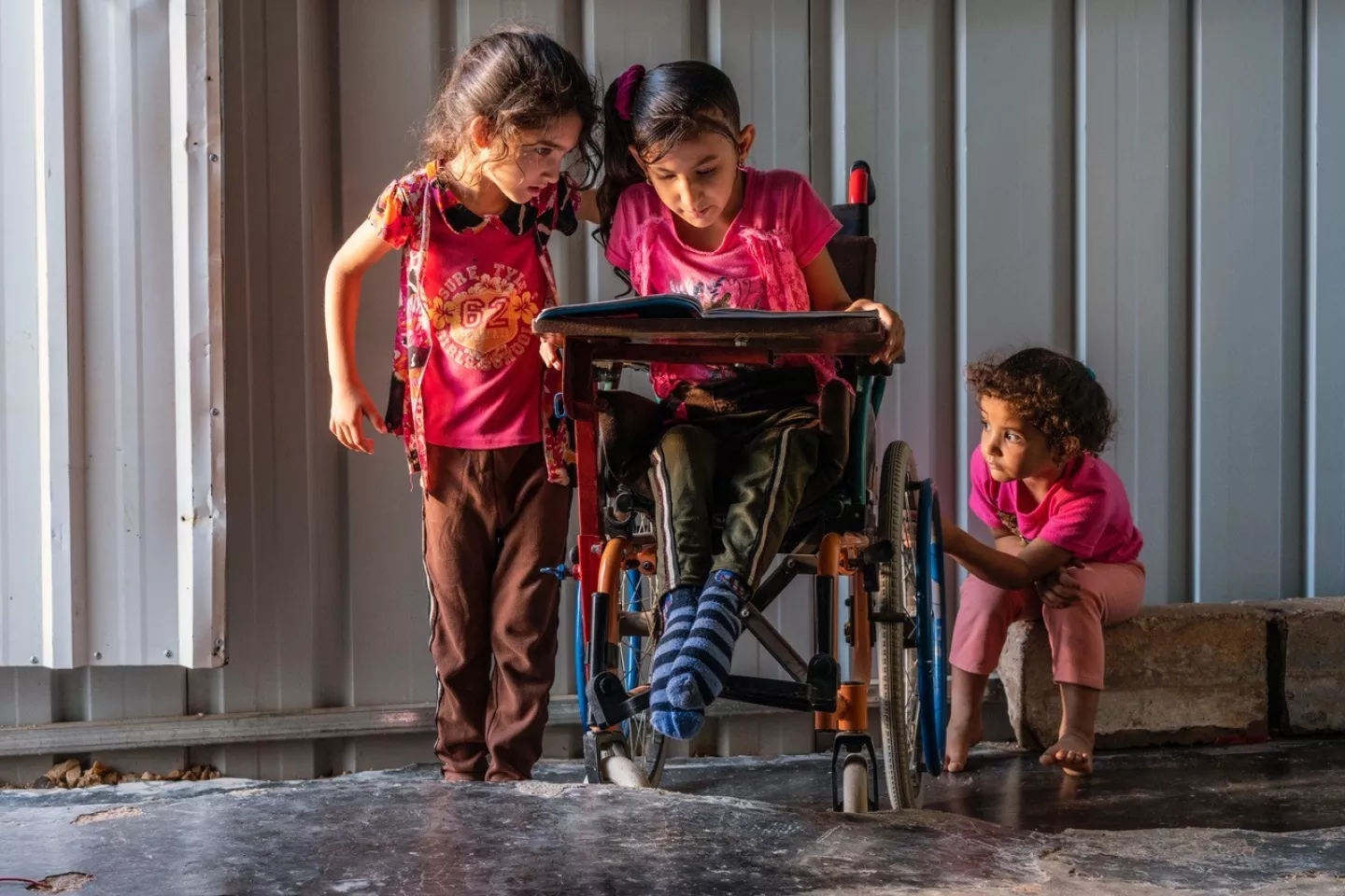 A disabled 8 years old girl sitting on a wheelchair reading with her two sisters 