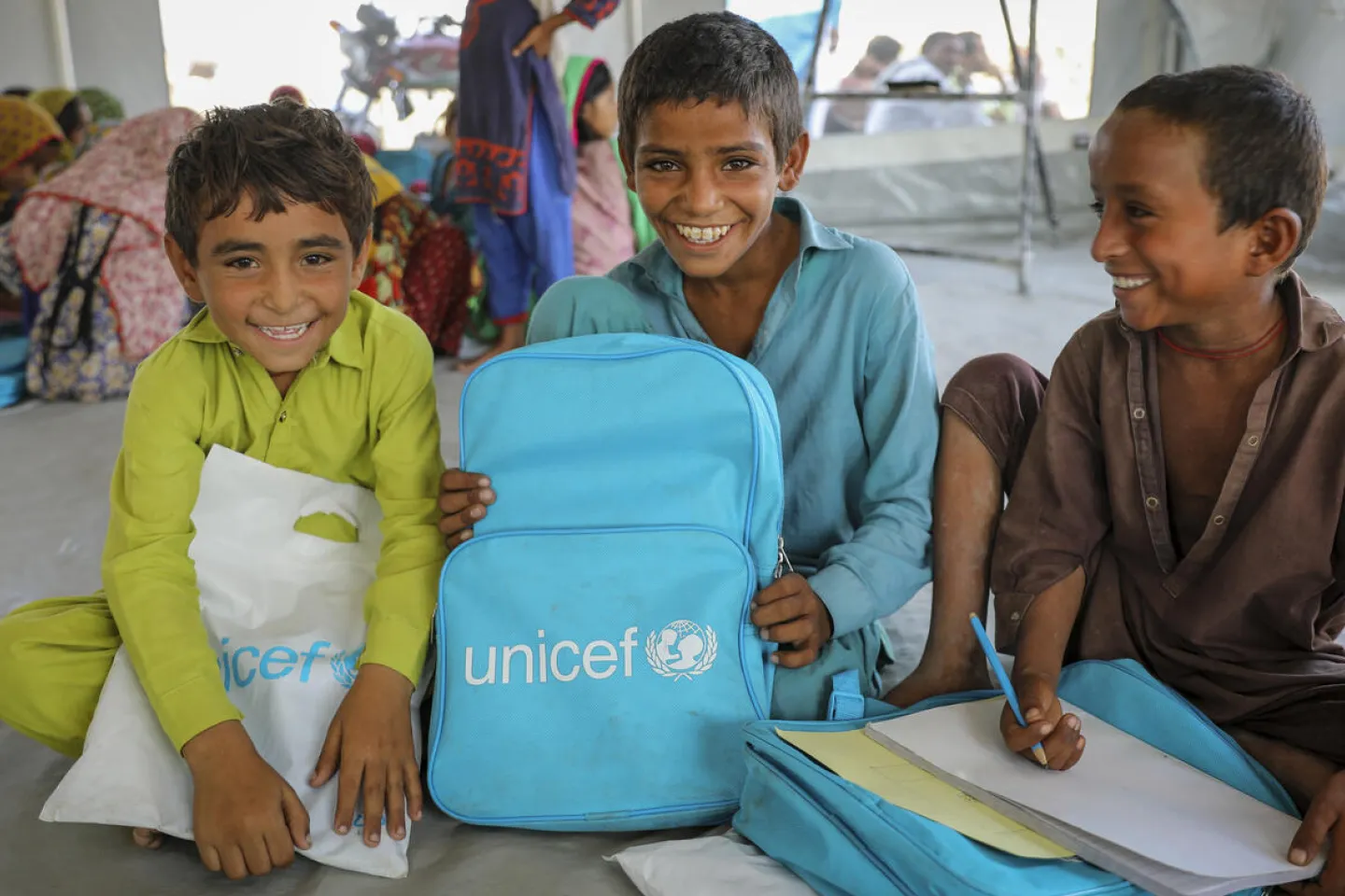 Pakistan, October 2022. (left to right) Farid, 6; Kashif, 8; and Muhammad Hussain, 7, participate in a class at a UNICEF-supported Temporary Learning Centre for children affected by recent floods.