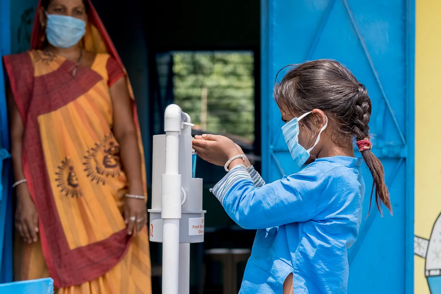 Payal Patel, six years old, uses a foot pedal sanitizer installed outside the AW before entering. Anganwadi workers (AWW) guiding children to use sanitizers and the correct way of wearing masks. 