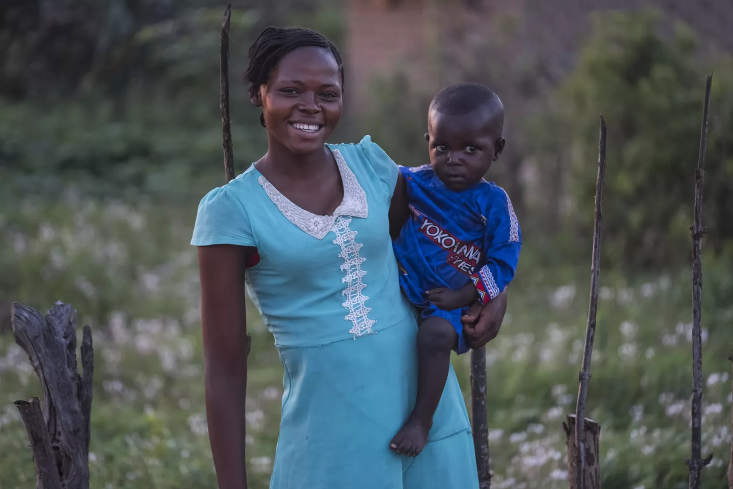 An adolescent girl smiles as she carries a young boy on her hip.