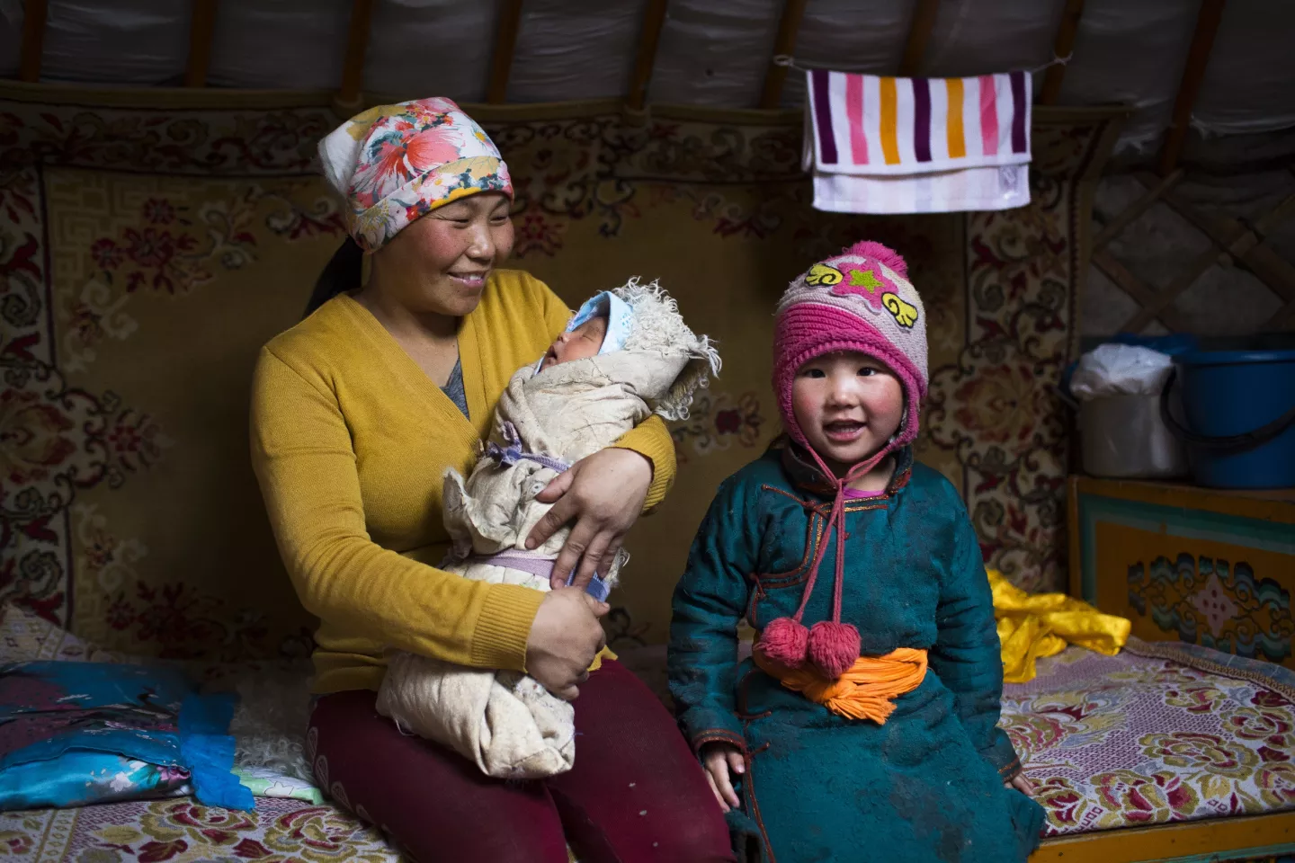 A mother holding her baby sits next her daughter.