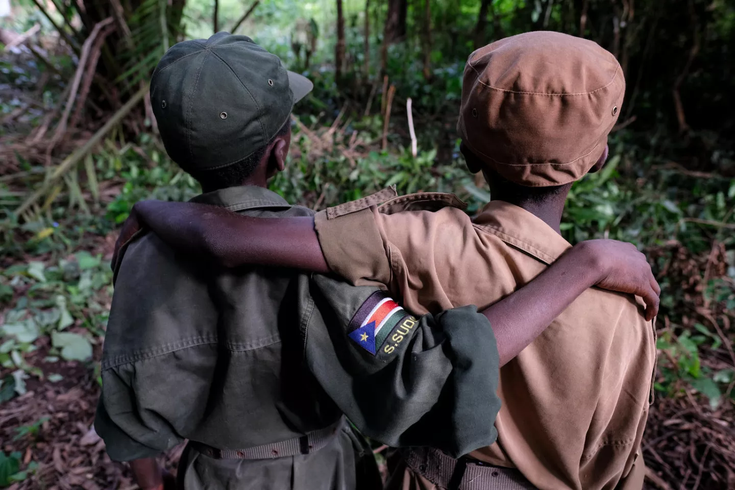 Two child soldiers in South Sudan stand with their backs to the camera, arms wrapped around each other, in 2018.