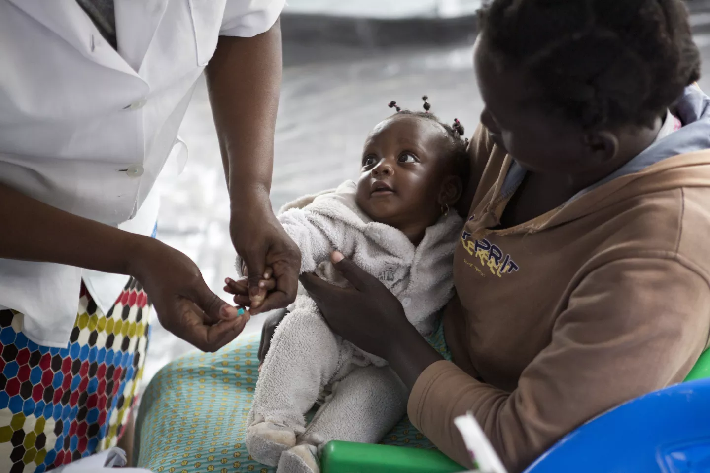 A mother holds her six-month-old daughter in a medical clinic as a health worker tests the baby for malaria.