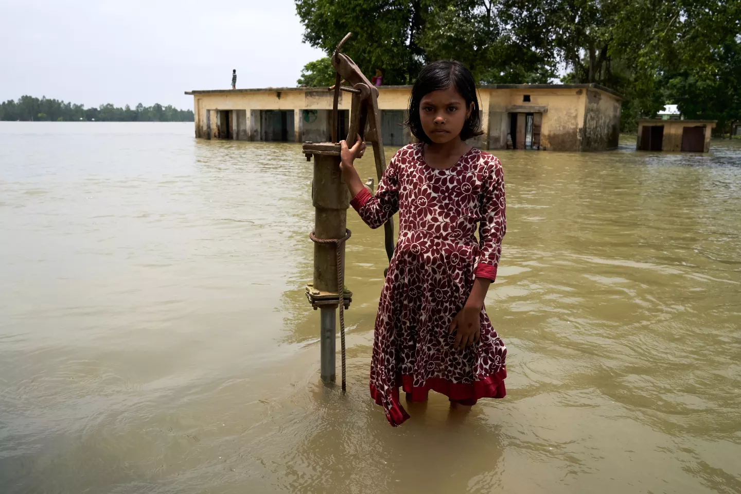 A girl stands in front of her school in Bangladesh that has been submerged under water. The well she stands upon is the only source of clean water in the area.