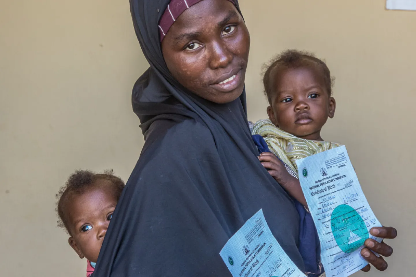 A woman with one child on her hip and one on her back holding birth certificates