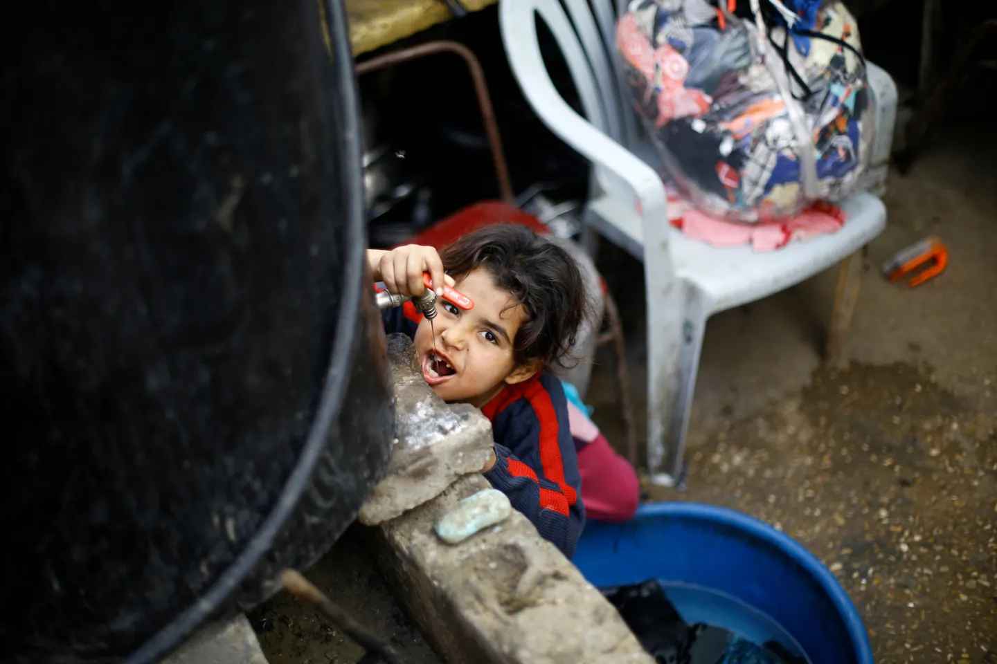 Eight-year-old Sawsan drinks water from a container outside the tin-roofed shack